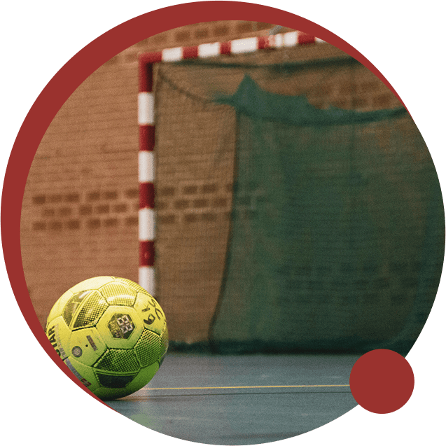 A yellow ball near an indoor futsal goalpost with net.